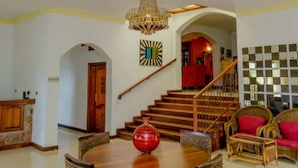 A spacious living room with a wooden dining table surrounded by wicker chairs, a chandelier, and a staircase leading to an upper level. - Select Boutique Hotel (Kigali)