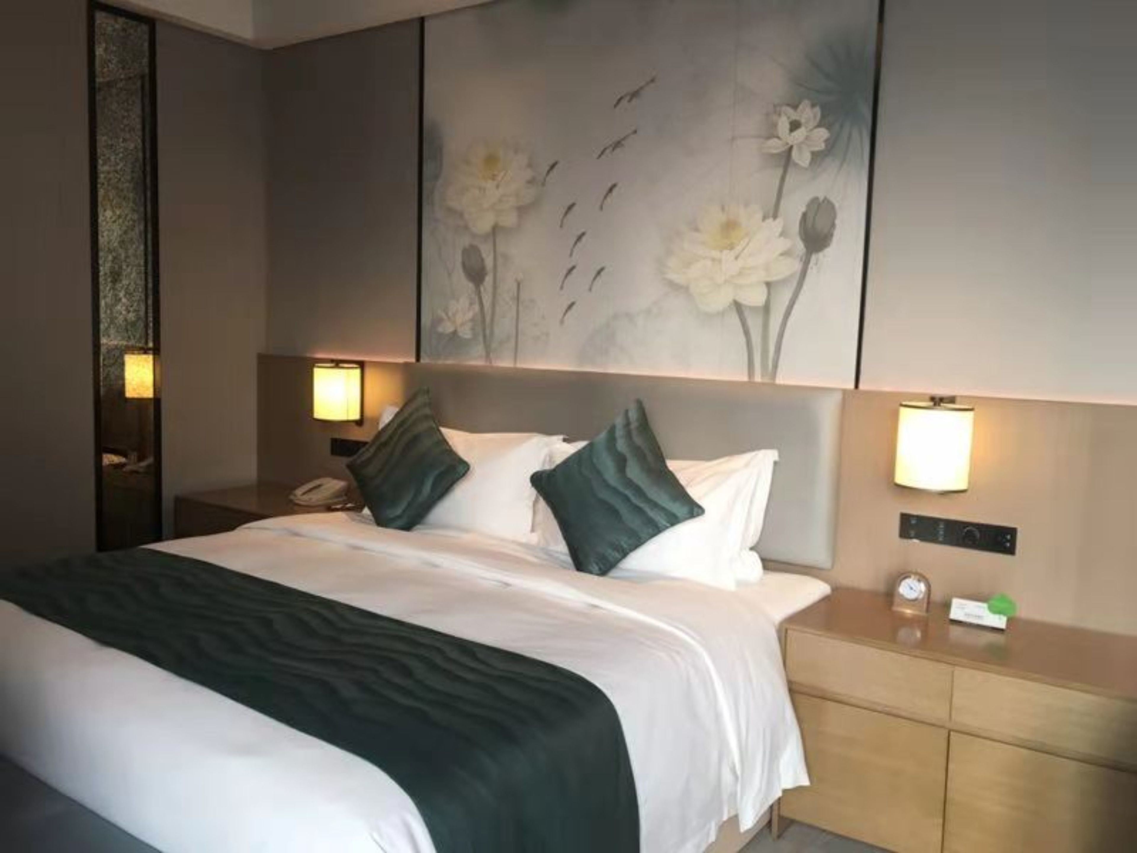 A hotel room with a large bed, two bedside tables, a nightstand, and a wall-mounted lamp.