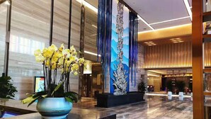 A modern lobby with a marble reception desk, a large vertical sculpture, and a blue wall with a mountain landscape mural. - Courtyard by Marriott Hangzhou Xiaoshan (Hangzhou)