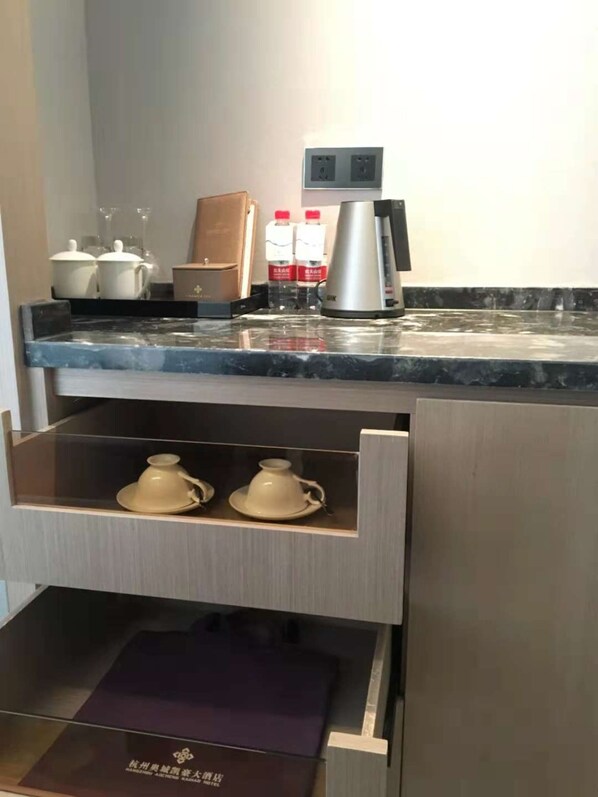 A kitchen with a marble countertop, two white teapots, a coffee maker, and a drawer with a purple interior.