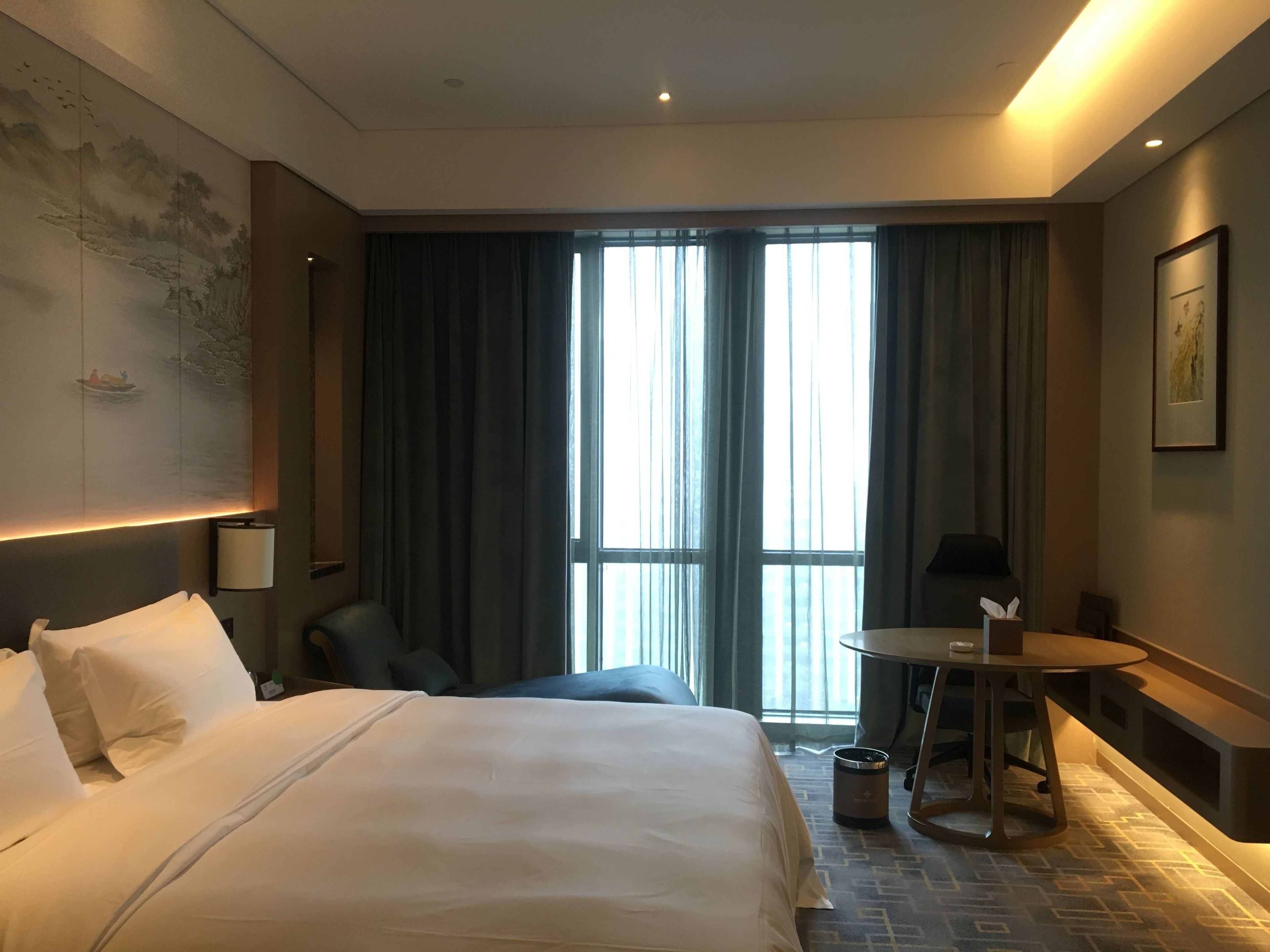 A hotel room with a large bed, a desk, and a view of the outdoors through the window.