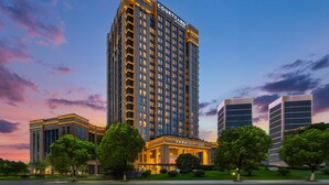 A high-rise hotel with a prominent 'Courtyard' sign, surrounded by well-maintained greenery and a clear sky. - Courtyard by Marriott Hangzhou Xiaoshan (Hangzhou)