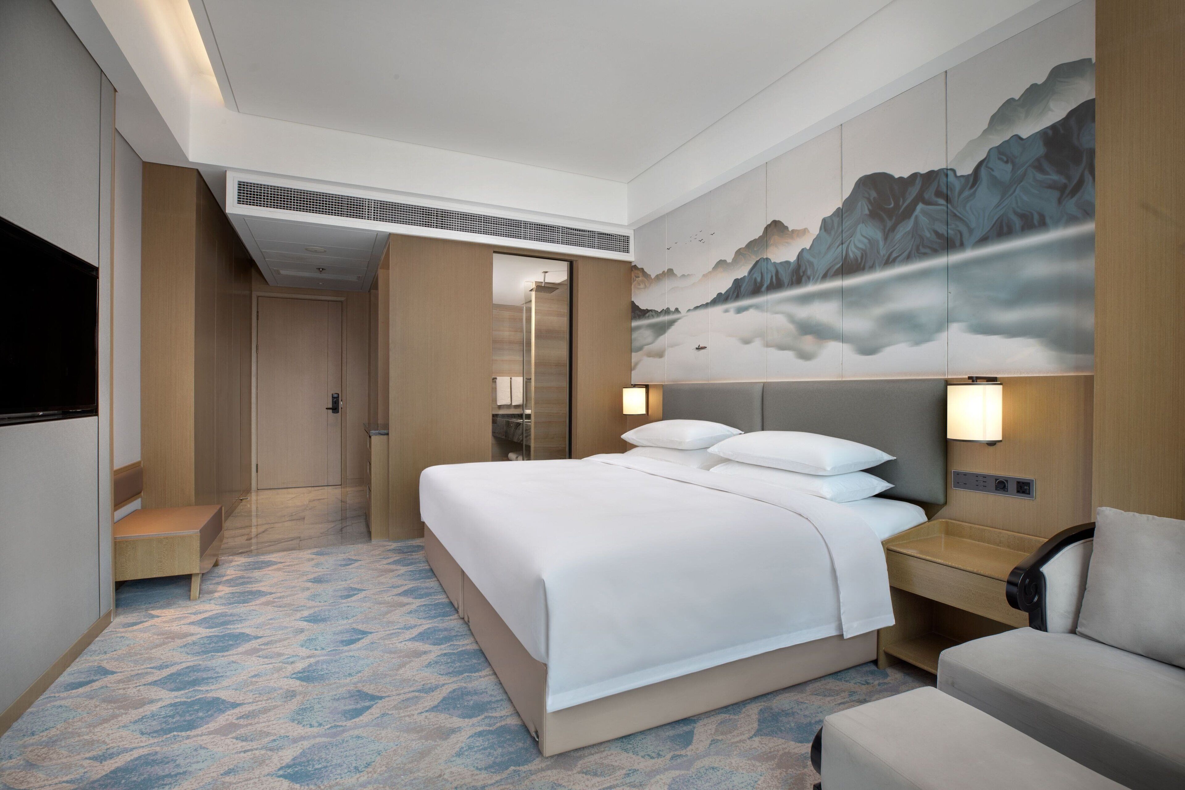 A hotel room with a large bed, bedside tables, a TV, and a wall-mounted artwork.