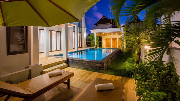 A modern outdoor pool area with a wooden deck, lounge chairs, and a green umbrella. - Villa Palavee A2 (Krabi)