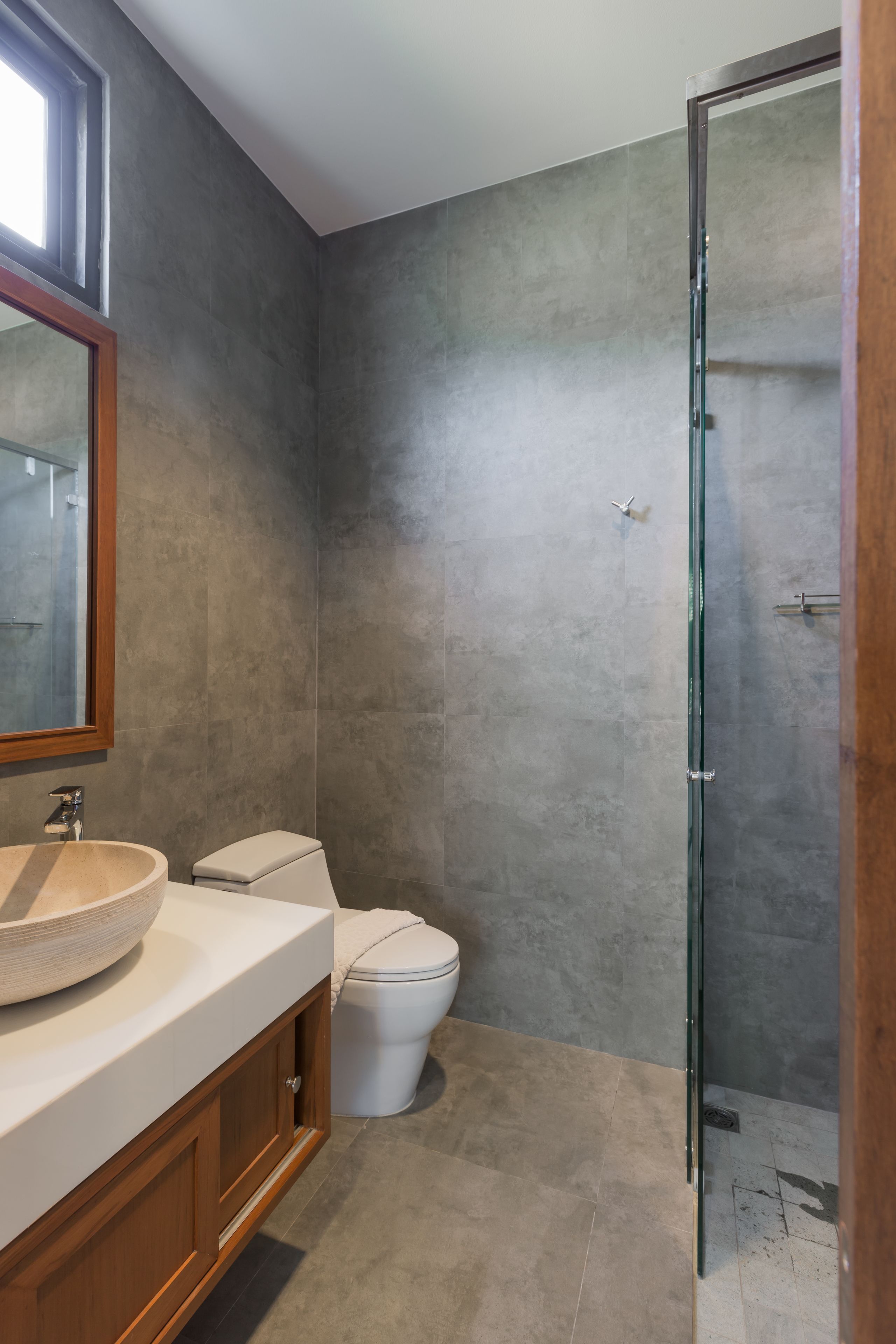 A modern bathroom with a large mirror, a round sink, a toilet, and a glass shower enclosure.