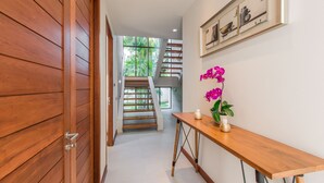 A hallway with a wooden door, a staircase, and a wooden table with a vase of flowers. - Villa Palavee A2 (Krabi)