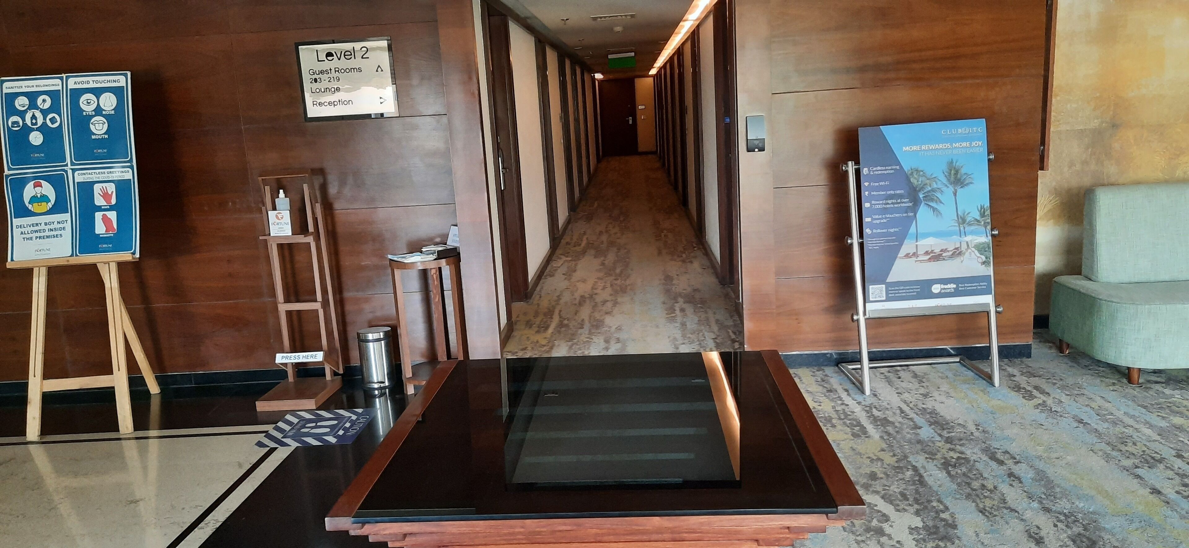 A hotel corridor with a reception desk, directional signs, and a lounge area.