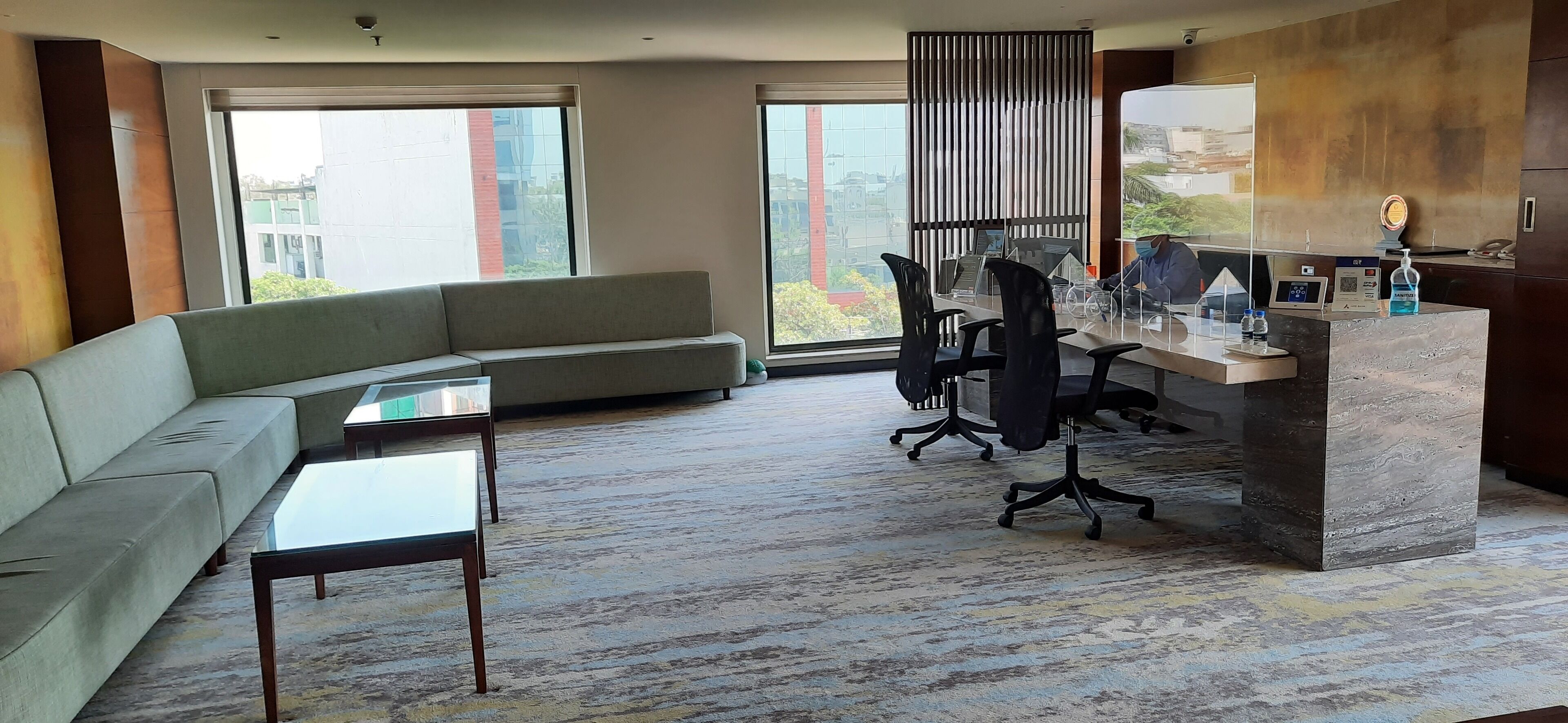 Habitación de hotel moderna con sofá, una mesita, un escritorio con sillas y grandes ventanales con vistas a la ciudad.