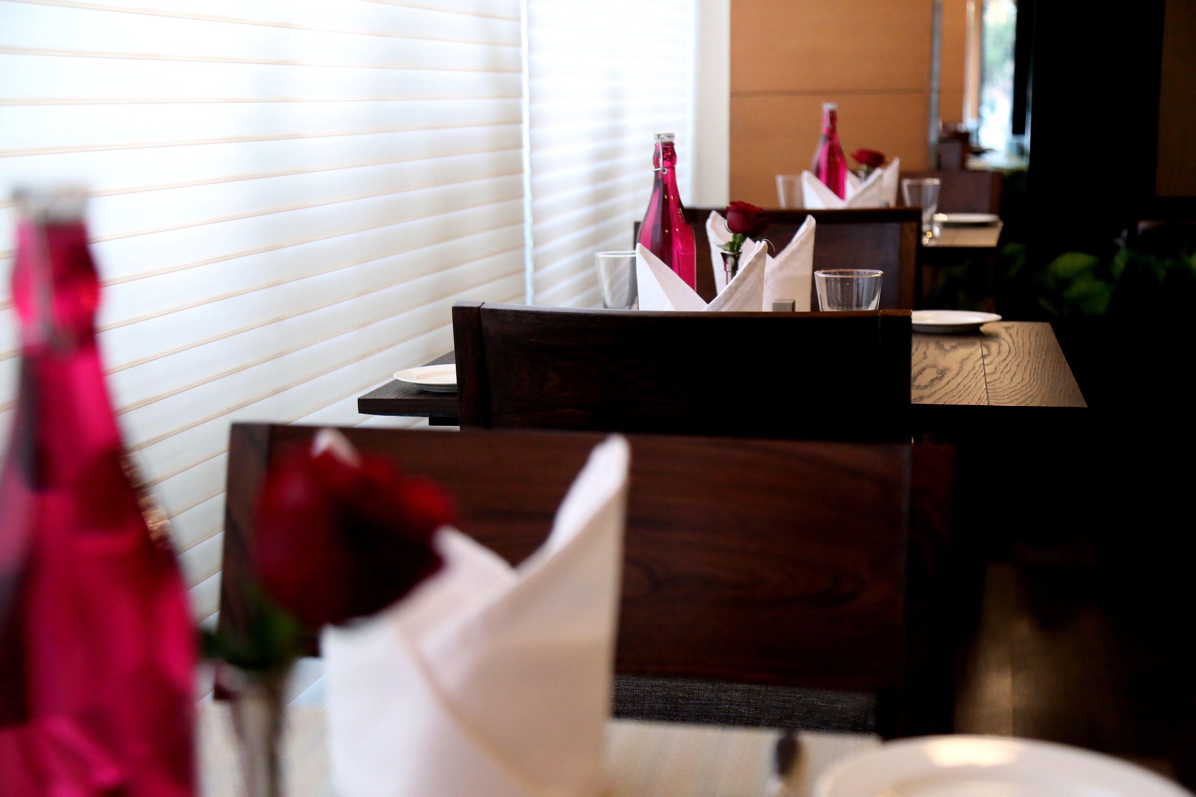 Un comedor con mesas de madera, servilletas blancas y una botella de vino tinto.