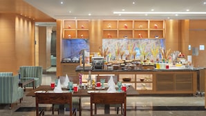 Un moderno vestíbulo de hotel con zona de buffet, arreglos de asientos y una pared decorativa con fuente de agua.