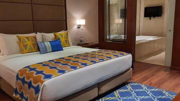 A hotel room with a large bed, a nightstand, a bedside table, a window with blinds, and a bathroom visible through the door.