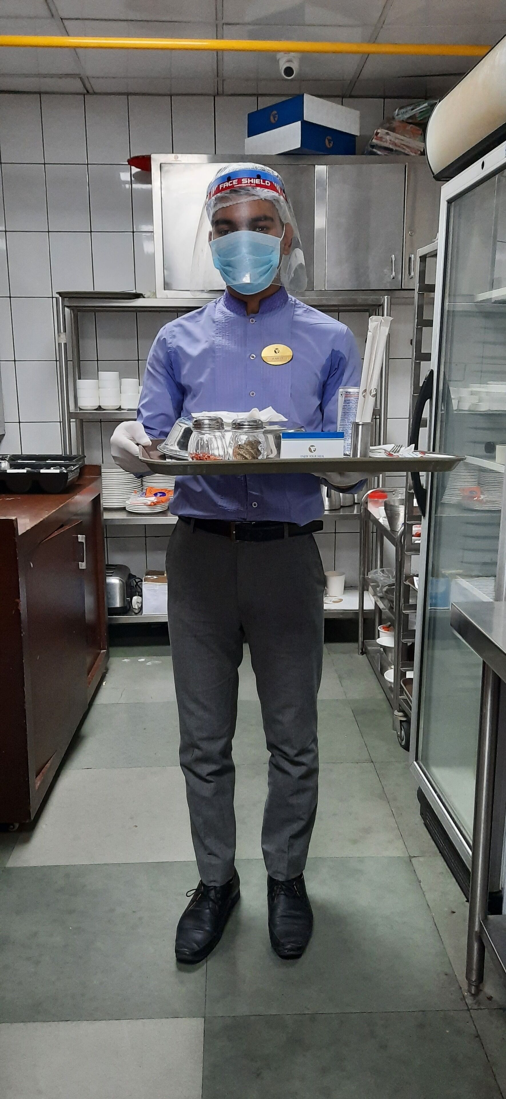 Una persona con uniforme azul lleva una bandeja con salsas y aderezos en una cocina.
