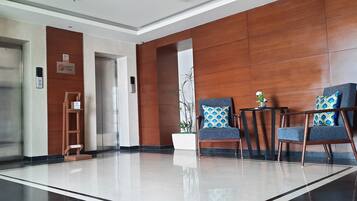 A modern lobby with two elevators, a reception desk, and a seating area with patterned cushions.