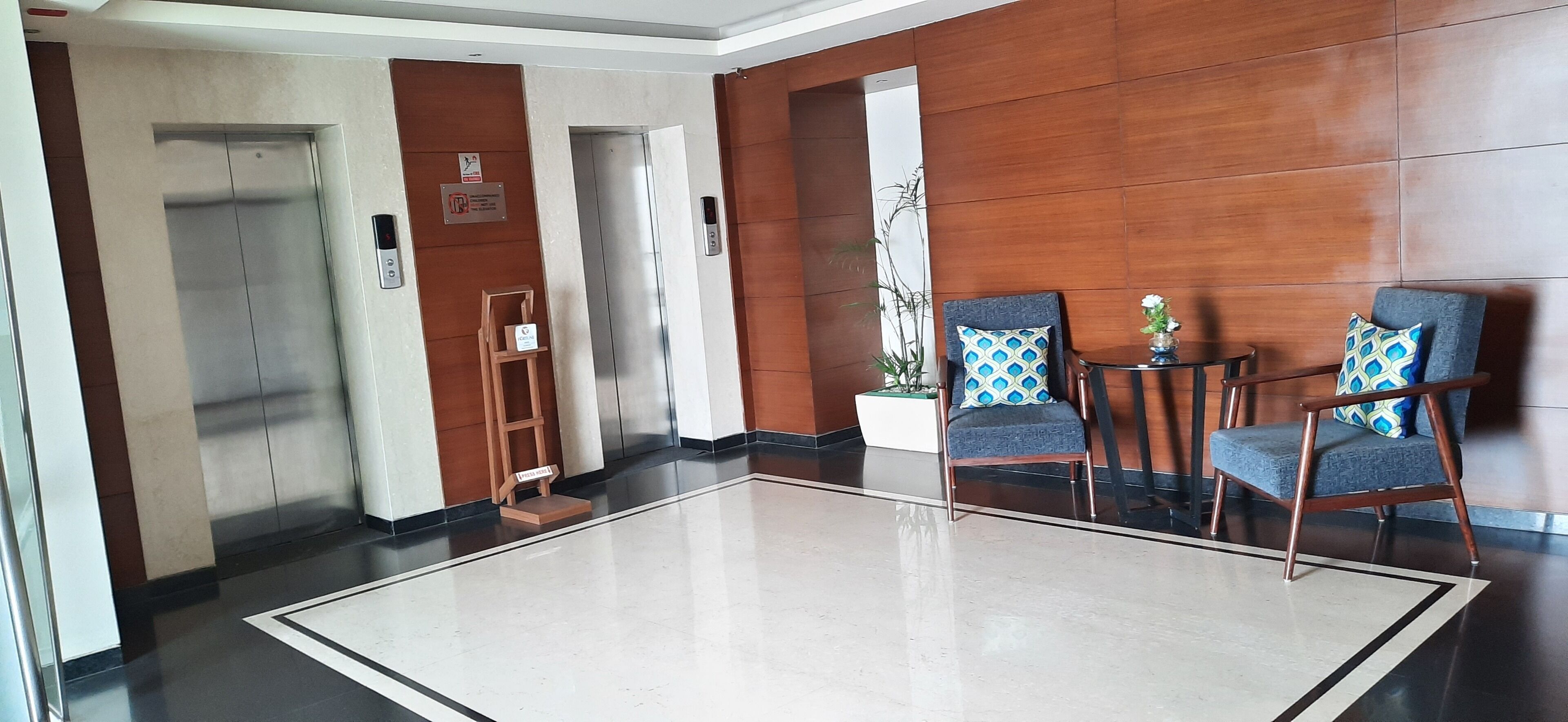 A lobby with two elevators, a reception desk, and a seating area with chairs and a small table.