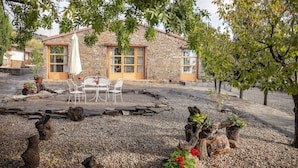 Un edificio de piedra con un patio que incluye una mesa y sillas, rodeado de grava y elementos de madera decorativa.