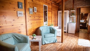 Interior acogedor de una cabaña de madera con dos sillones azul claro, una mesita blanca y un refrigerador.