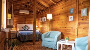Acogedora habitación de cabaña de madera con una cama, dos sillones, una mesita y una planta en maceta.