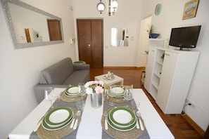Un coin repas avec une table dressée pour quatre personnes, un canapé, un téléviseur et une porte au fond.