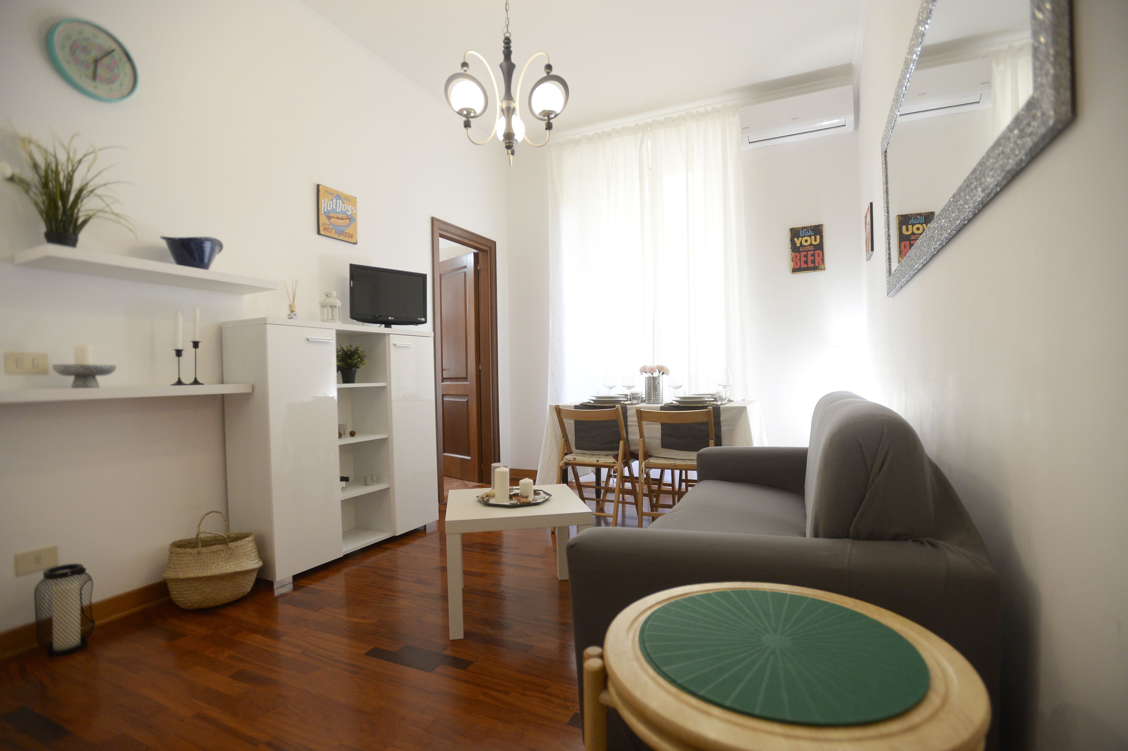 A living room with a sofa, a dining table with chairs, a chandelier, and a television on a shelf.