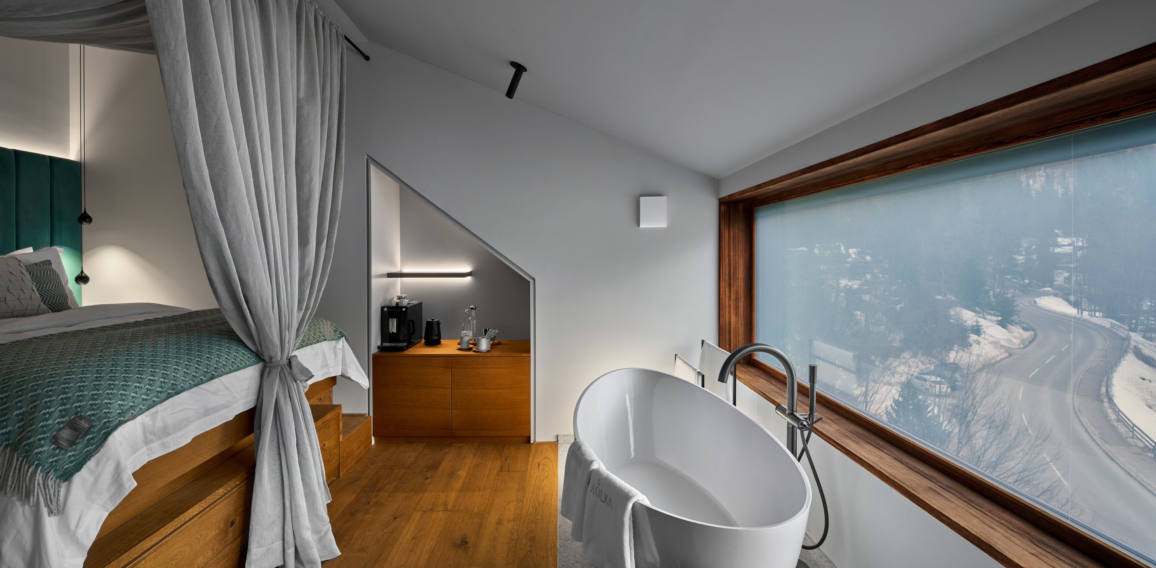 Quarto moderno com uma cama grande, uma penteadeira com espelho, uma banheira e vista para uma paisagem coberta de neve.