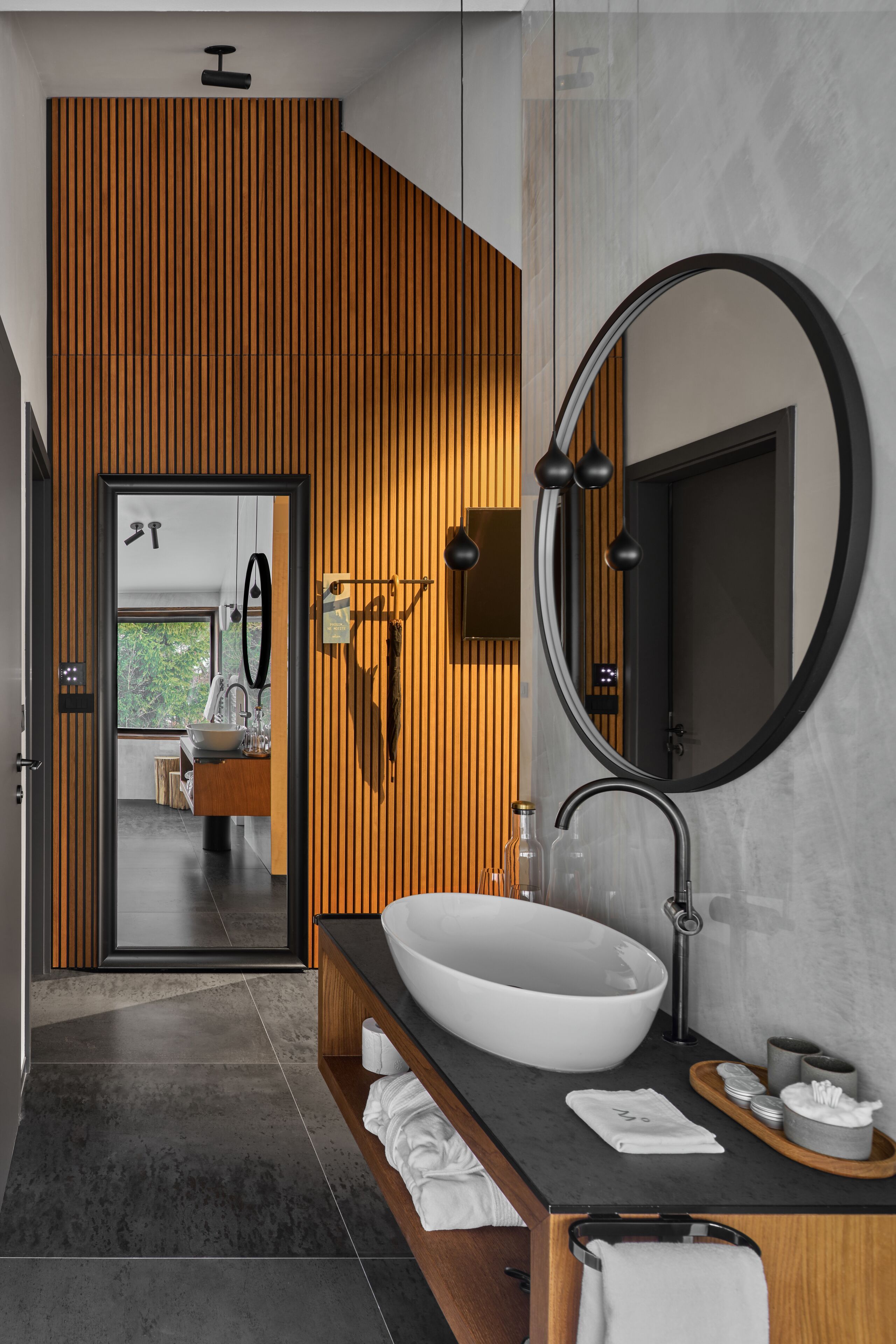 Un baño moderno con un lavabo ovalado grande, un espejo redondo y paneles de madera en la pared.