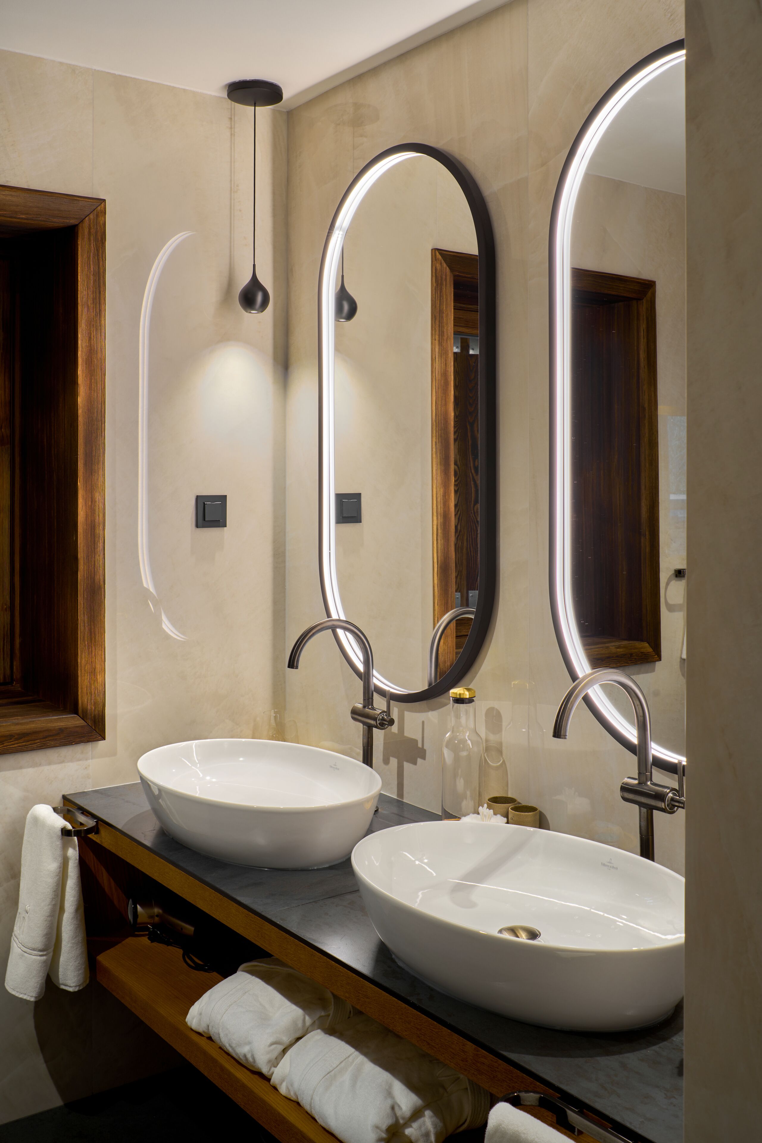 Ein modernes Badezimmer mit zwei Waschbecken, einem Holz-Badmöbel und drei Spiegeln.