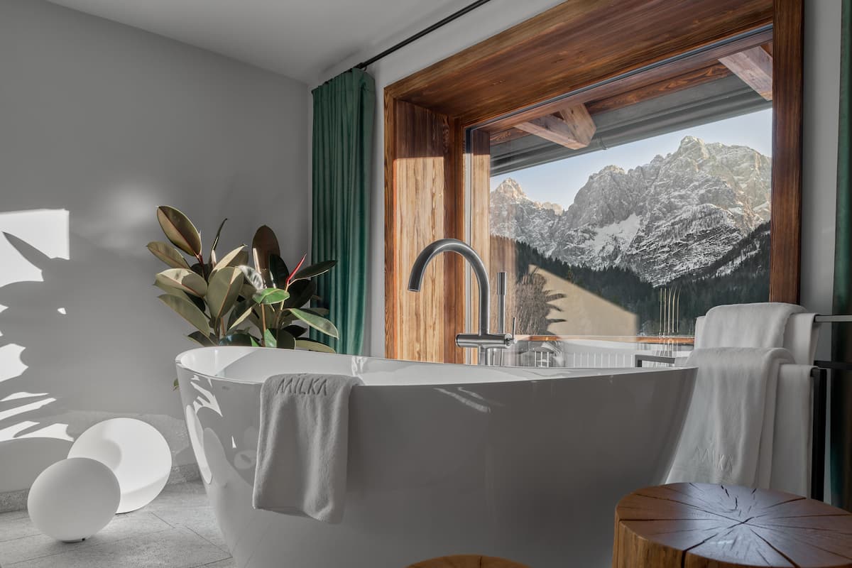 Une salle de bain moderne avec une baignoire sur pieds, un meuble-lavabo en bois et une vue sur des montagnes enneigées, visible à travers une grande fenêtre.