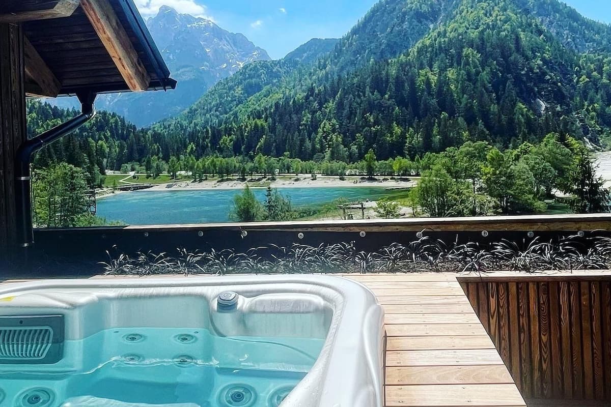 Une terrasse en bois avec un jacuzzi donnant sur un lac et des montagnes.