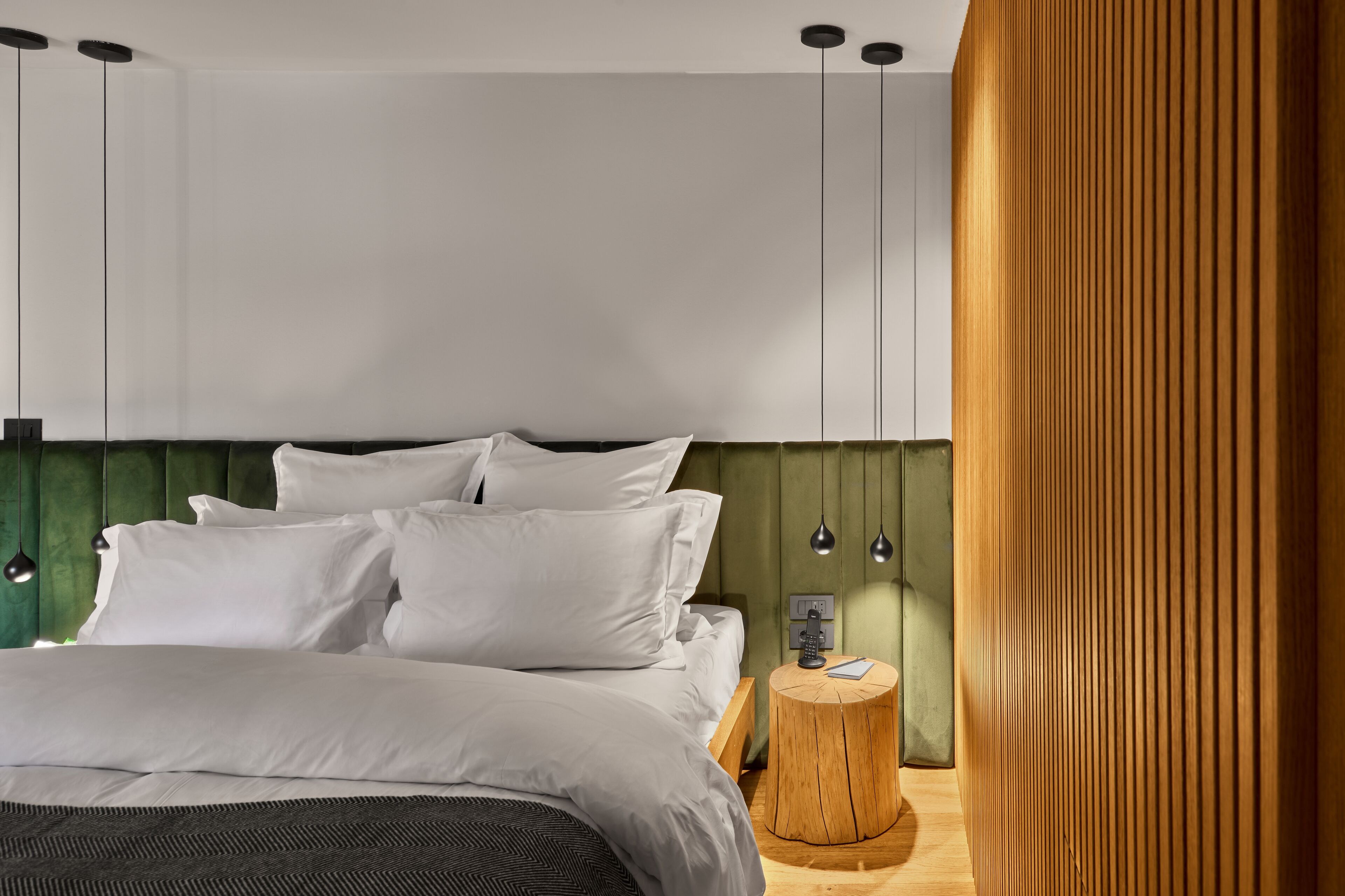 Un dormitorio moderno con cama, ropa de cama blanca, una mesita de noche de madera y un cabecero verde.