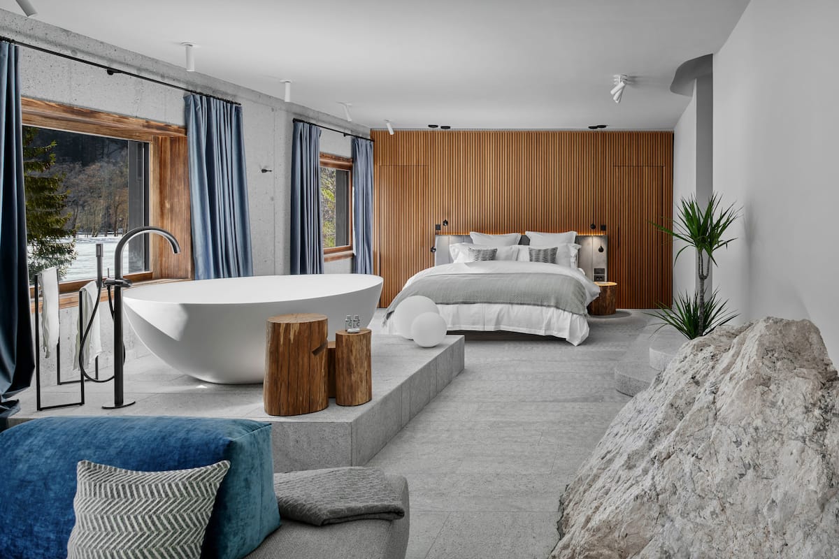 Une chambre moderne avec une grande baignoire, un lit avec une literie blanche et une vue sur un paysage enneigé par la fenêtre.
