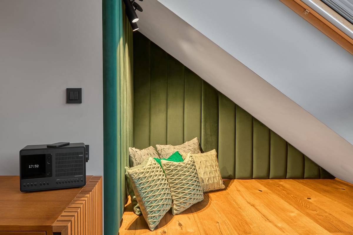 Une chambre moderne avec un plafond en pente, une table de chevet en bois, une radio et des coussins décoratifs.