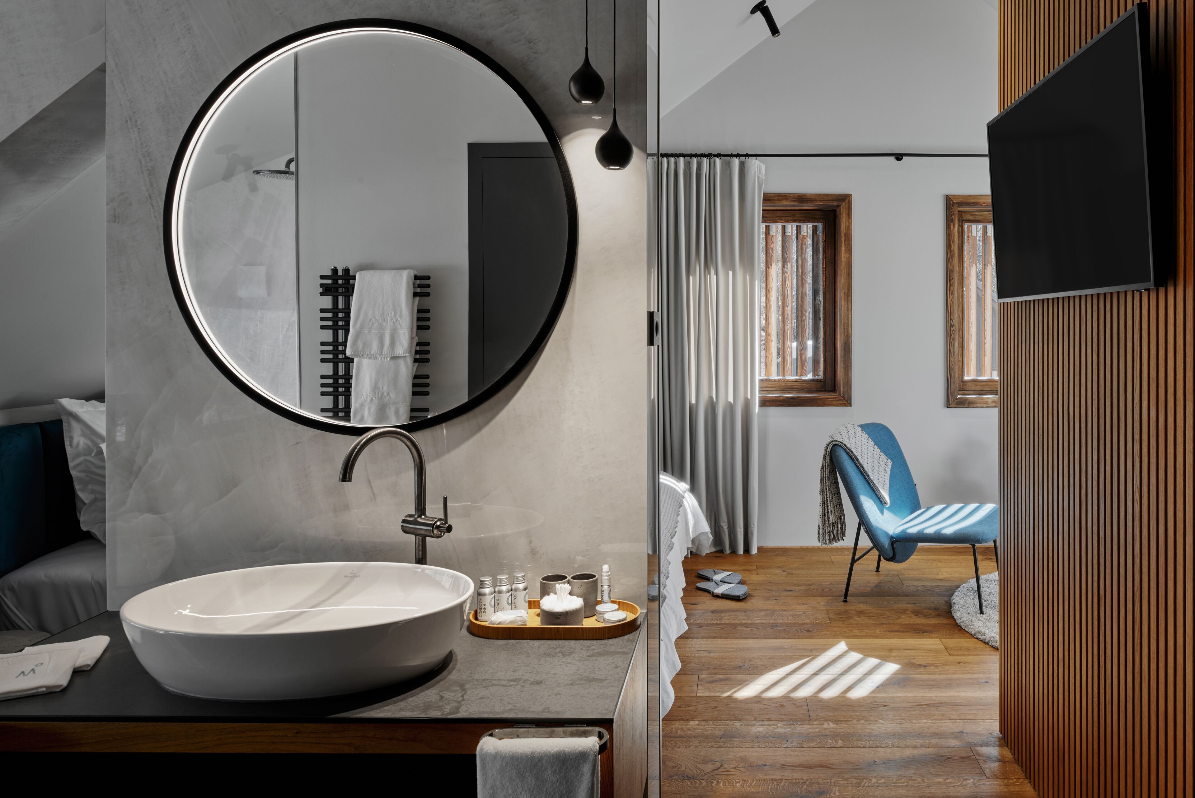 Un baño moderno con un espejo redondo grande, un lavabo blanco y un mueble de tocador de madera.