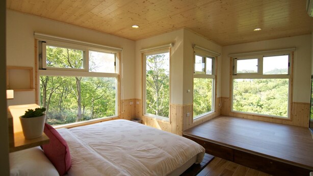 A bedroom with a large bed, wooden ceiling, and multiple windows offering a view of greenery. - I Sky Villa (Zaoqiao)