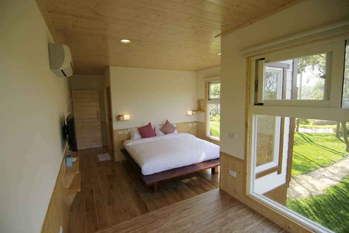 Een slaapkamer met een groot bed, houten vloeren, een raam en een deur naar een andere kamer.
