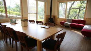A dining area with a wooden table and chairs, a red sofa, and large windows with a view of greenery. - I Sky Villa (Zaoqiao)