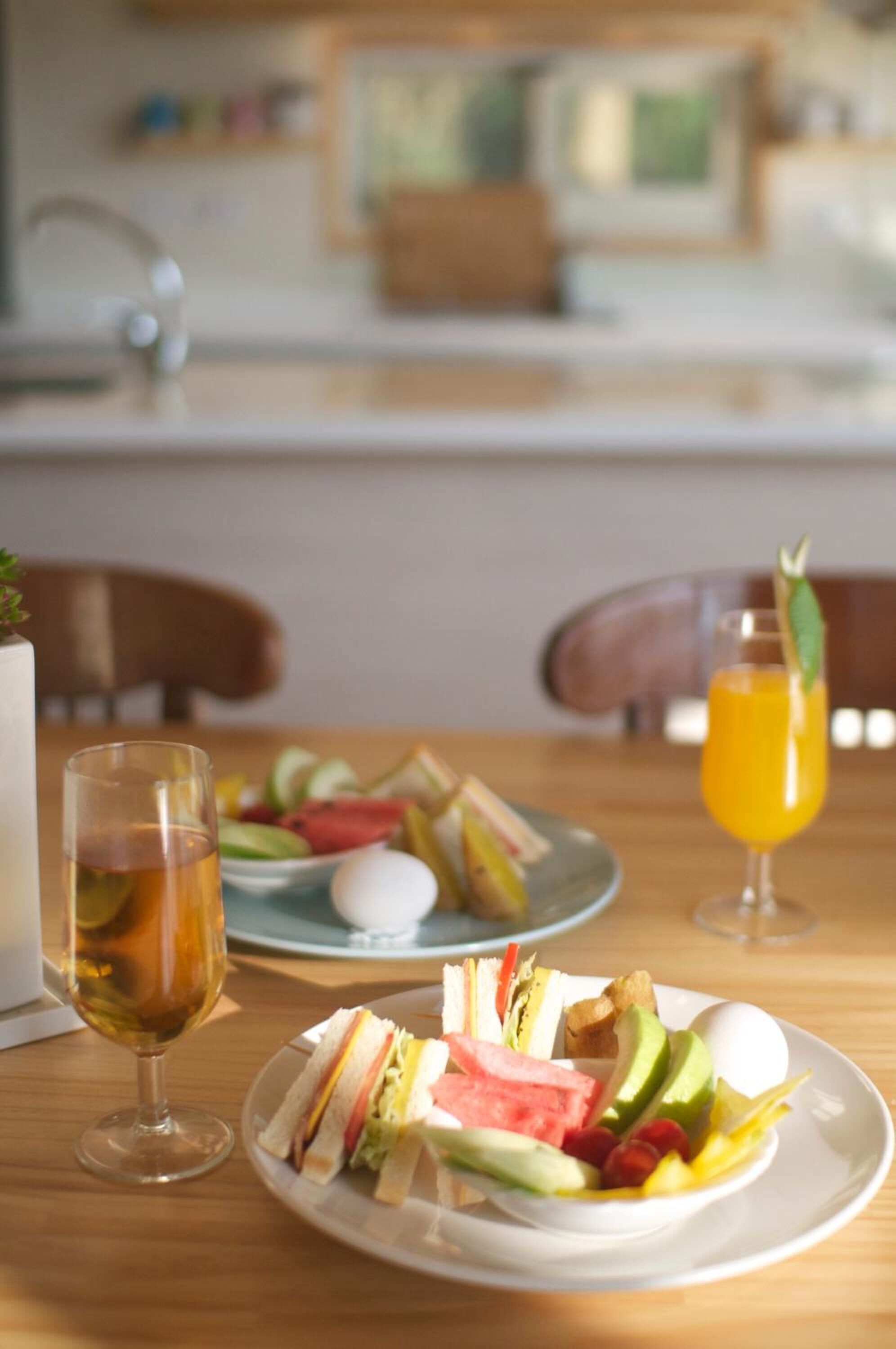 A breakfast setting with sandwiches, fruits, and a glass of orange juice on a wooden table.