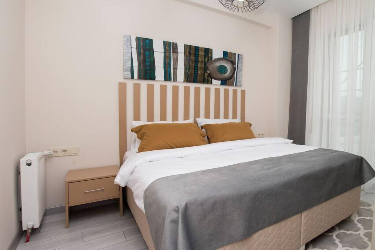 A modern bedroom with a bed, bedside tables, a radiator, and a window with curtains.