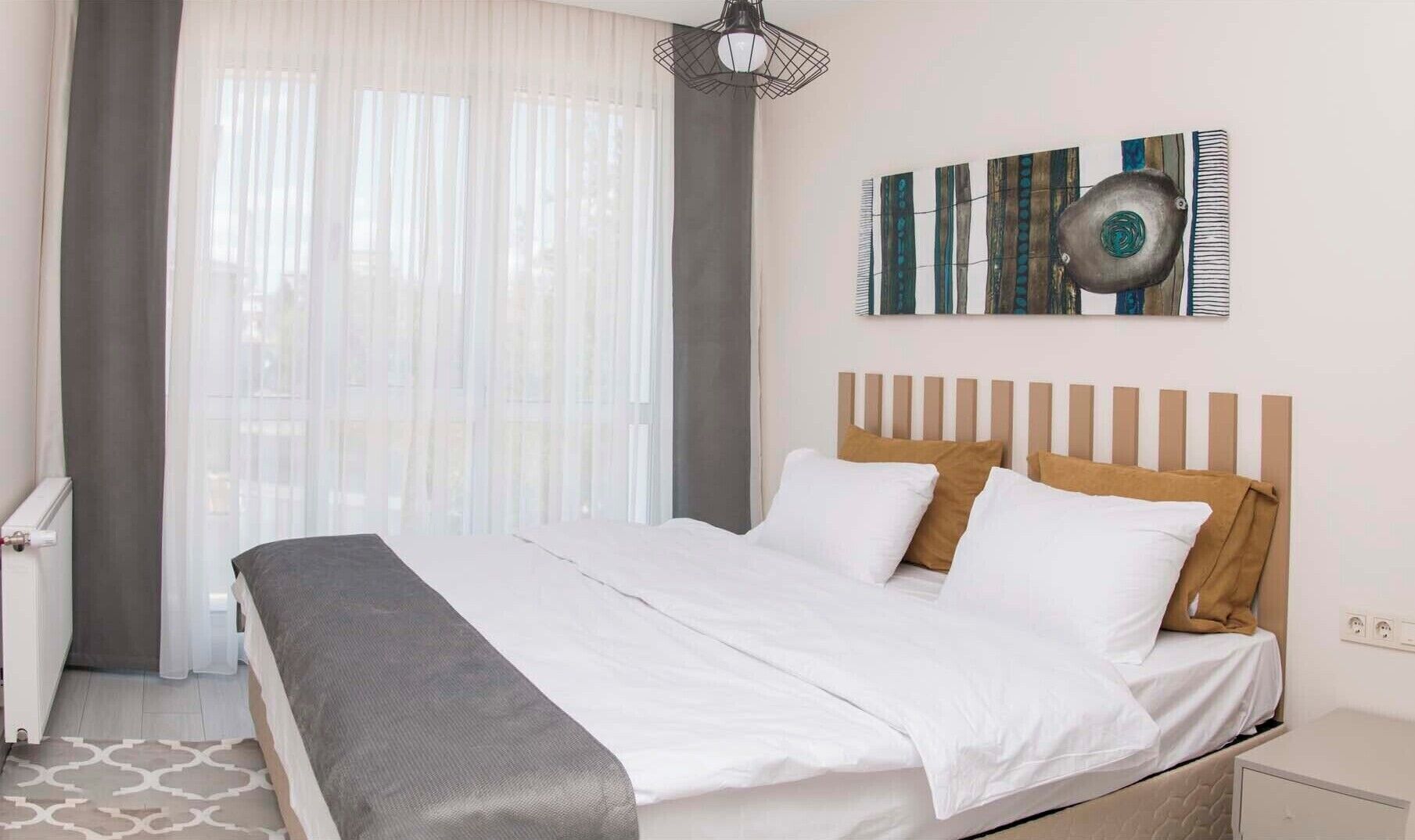 Une chambre d’hôtel avec un lit, une tête de lit, une table de chevet, une lampe et une fenêtre avec des rideaux.