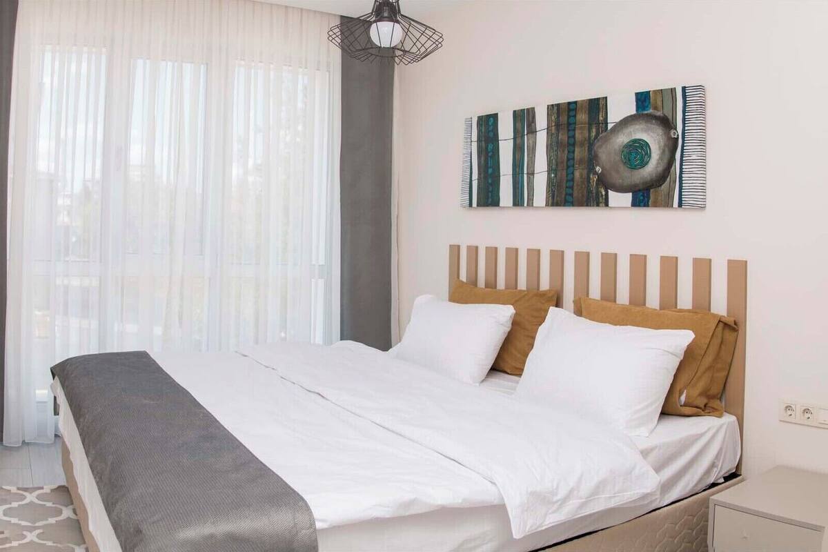 A hotel room with a bed, a headboard, a bedside table, a lamp, and a window with curtains.