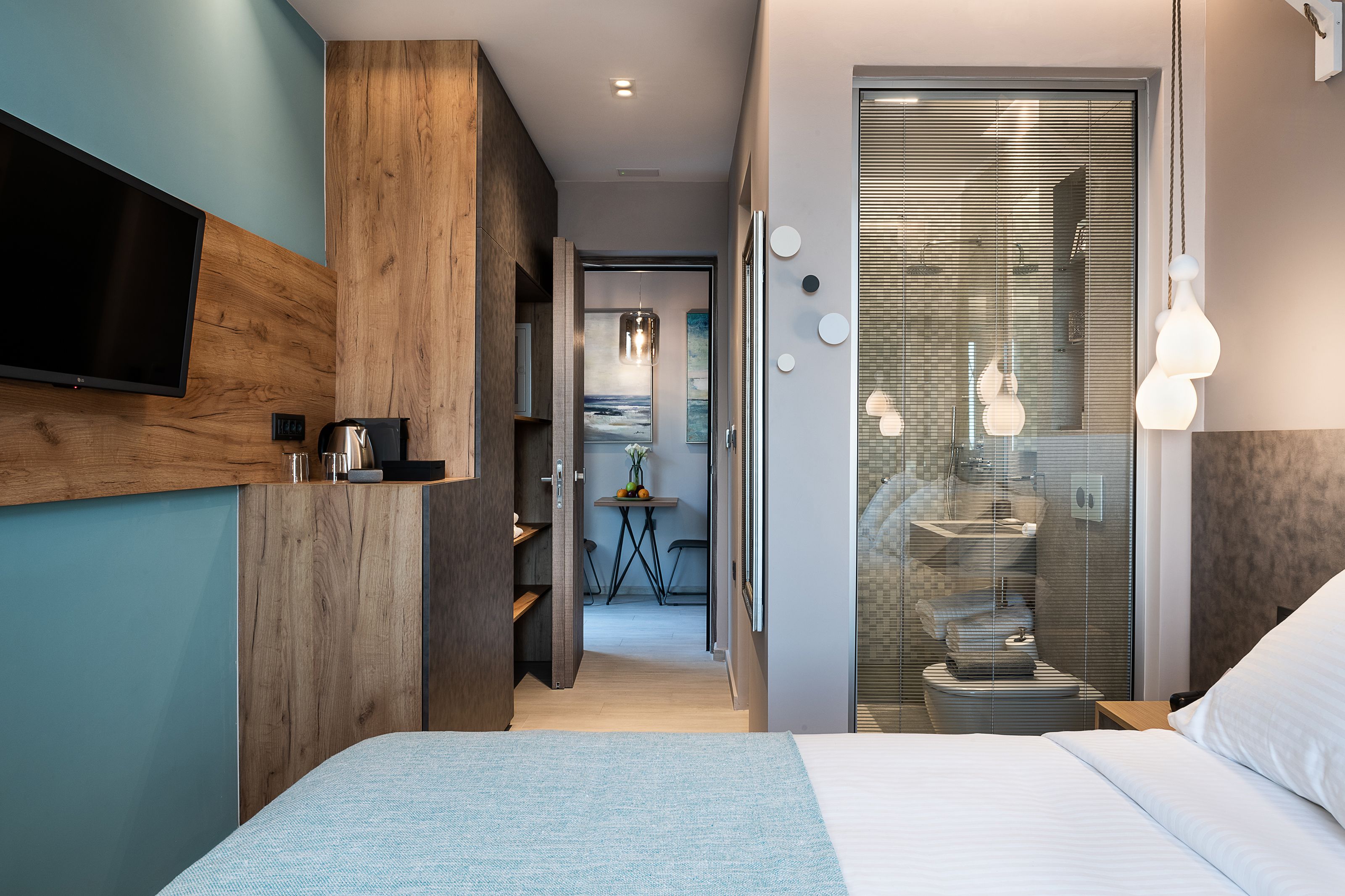 Una camera d'albergo moderna con un letto grande, una TV a schermo piatto montata a parete, un armadio in legno e un bagno con cabina doccia in vetro.