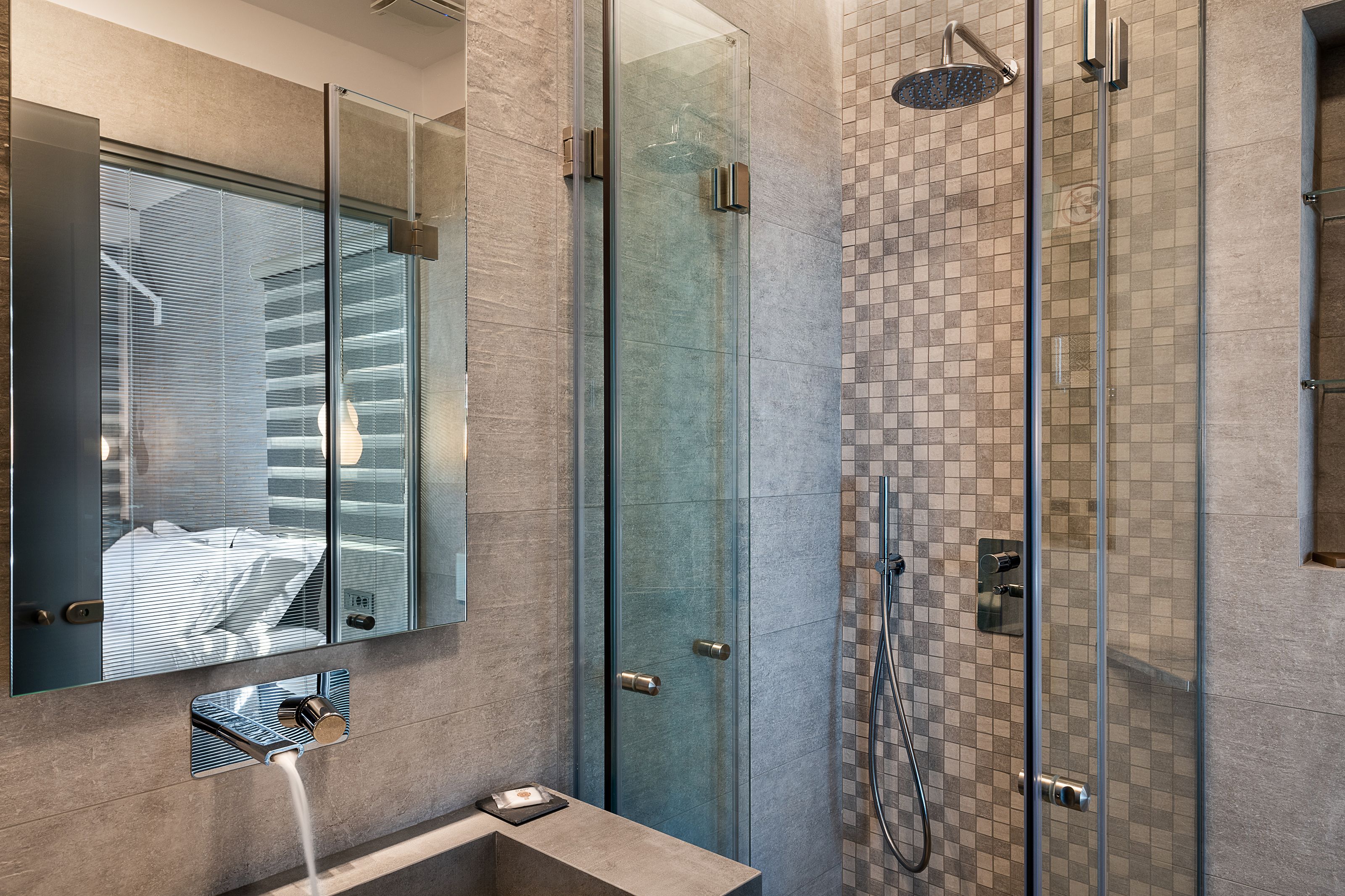 A modern bathroom with a glass shower enclosure, a large mirror, and a tiled wall.