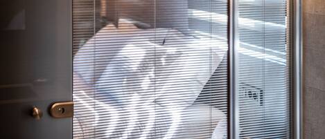 A door with a keyhole and a lock, leading to a room with a patterned floor and blinds partially covering a window.
