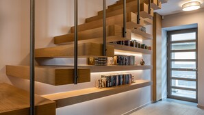 A modern staircase with wooden steps and metal railings, featuring built-in bookshelves and a door leading to a bright room. - Ciel Collection Suites (Chania)