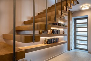 Una moderna scala con gradini in legno e ringhiere in metallo, con scaffali a muro e una porta che dà su una stanza luminosa.