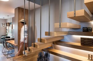 Un interno moderno con una scala in legno, un'area pranzo con sedie e tavolo, e una libreria piena di libri.