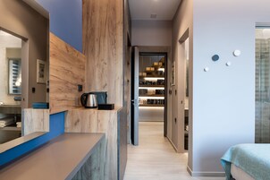 Hall moderna di un hotel con reception in legno, angolo cucina a vista e corridoio che porta a una camera da letto.