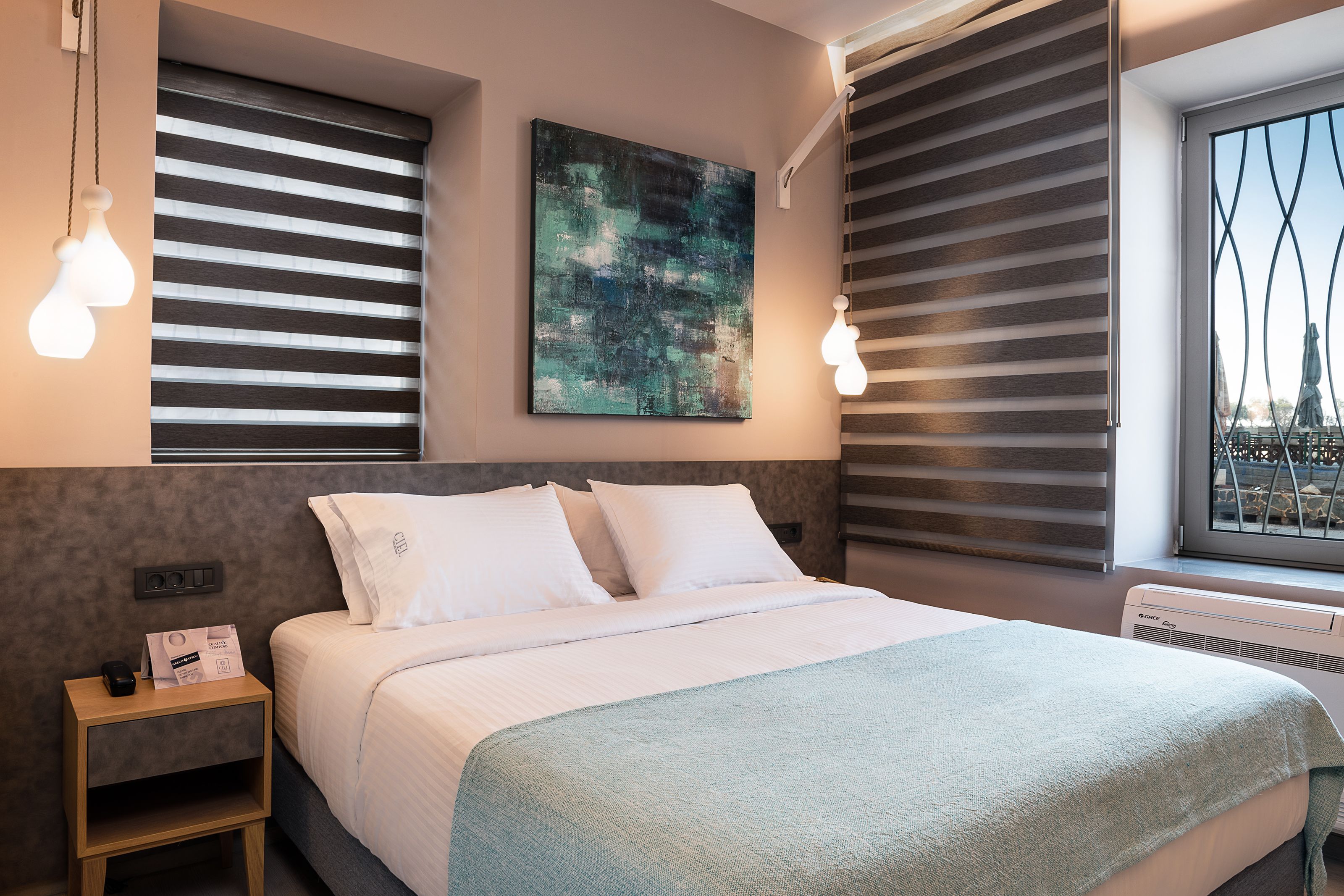 Una habitación de hotel moderna con una cama bien hecha, un cuadro abstracto grande en la pared y una ventana con persianas.