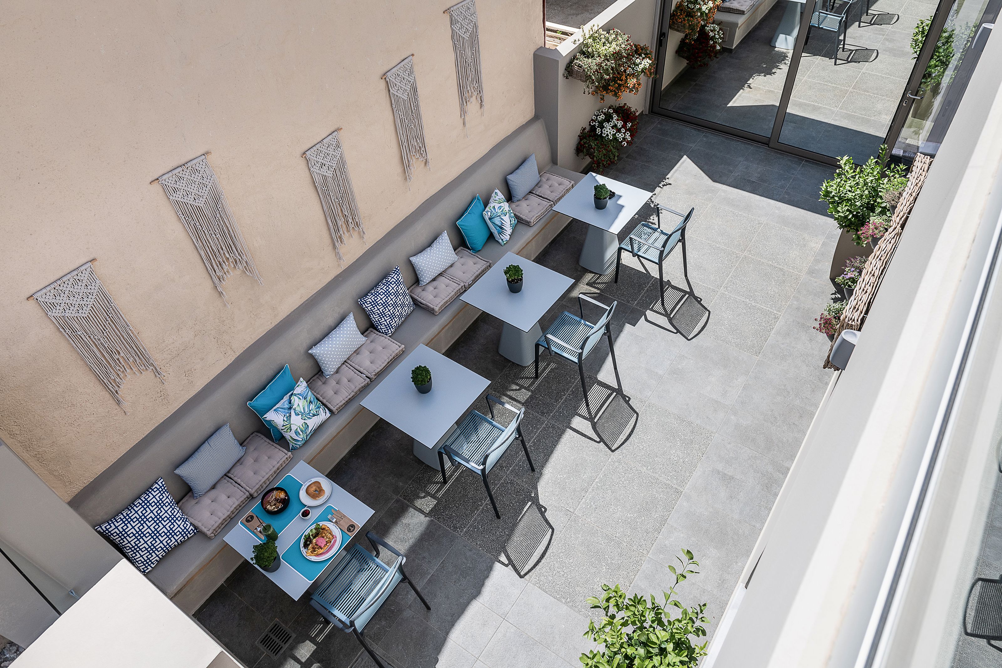 Un patio exterior con asientos y mesas, una pared decorada con macramé y plantas en macetas.
