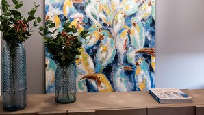 A reception desk with a colorful abstract painting, two glass vases with greenery, and pendant lights. - Ciel Collection Suites (Chania)