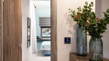 A hallway with a wooden door, a bed with a blue headboard, and two glass vases with green plants on a wooden shelf.